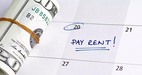 A calendar marked with "PAY RENT!" next to the 20th, accompanied by a roll of US dollar bills, reminds the viewer of an upcoming rent payment.