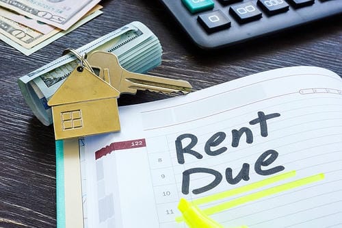 A notebook with "Rent Due" highlighted, alongside cash, a house-shaped keychain, and a calculator, symbolizes the financial obligation of paying rent.