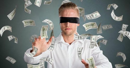 A blindfolded man surrounded by falling US dollar bills, reaching out as if to catch them.
