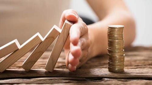 A hand stopping falling dominoes next to a stack of coins, symbolizing financial risk management.