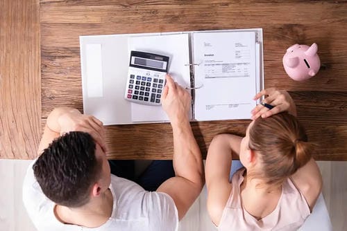 A couple reviewing finances with a calculator, documents, and a piggy bank on a wooden table.