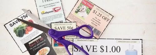 A pair of purple scissors cutting grocery coupons with savings offers like "SAVE 75¢" and "$1.25 OFF".