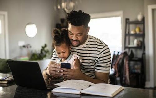 A father and daughter looking at a phone together while managing finances at home.
