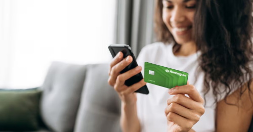 A woman using a Huntington bank card with her smartphone for mobile banking at home.