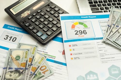 Credit reports showing low scores (296, 310) next to a calculator, cash, and laptop.
