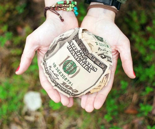 A pair of hands holding a ball made of folded US $100 bills.