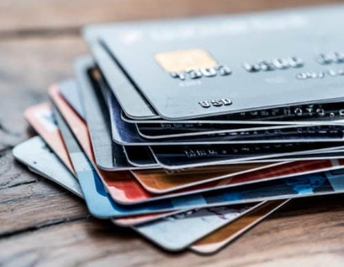 A stack of various credit cards resting on a wooden surface.