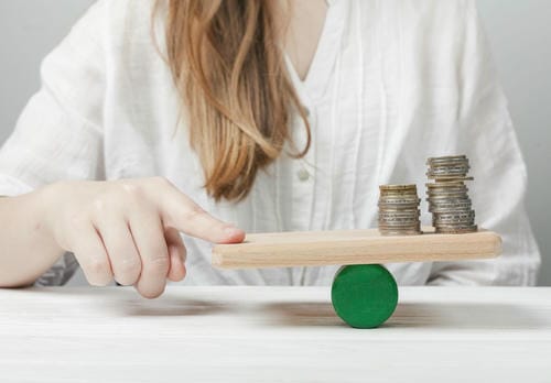 A woman balancing stacks of coins on a seesaw, representing financial balance and risk management.