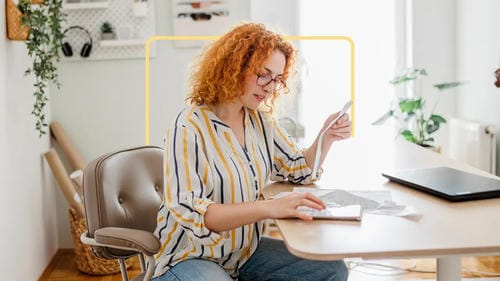A woman at her desk reviewing receipts and financial documents while using a calculator.