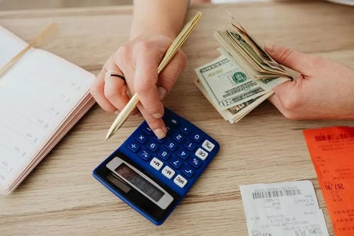 Hands using a calculator, holding cash, and managing receipts while budgeting personal finances.